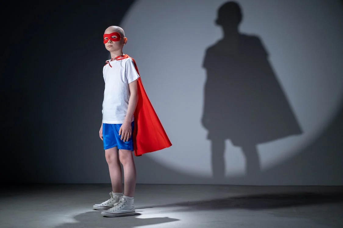 pexels-photo-6203476 Enfant malade qui a une cape de superhéro avec ombrage contre le mur