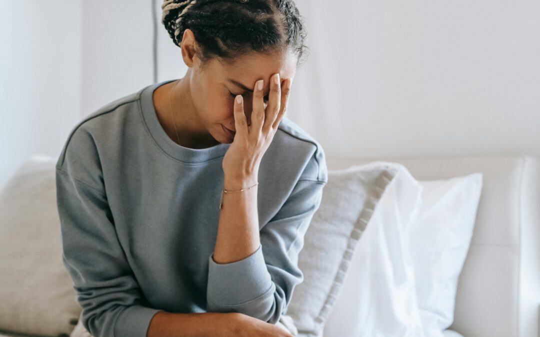 Femme avec le visage dans une main assise sur un lit qui semble au bout de ses forces (fatigue émotionnelle)