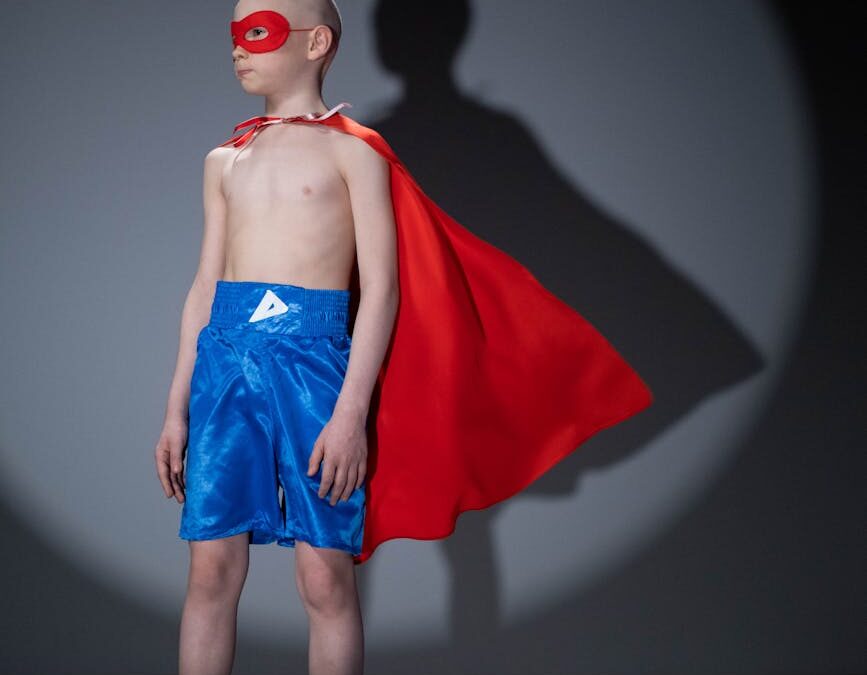shirtless child wearing a red cape and blue shorts